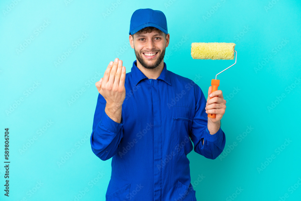 Painter caucasian man isolated on blue background inviting to come with hand. Happy that you came