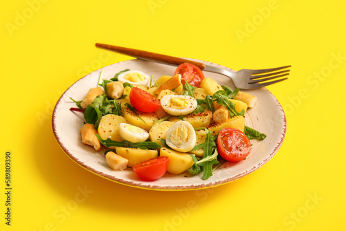 Plate of tasty potato salad with eggs and tomatoes on yellow background