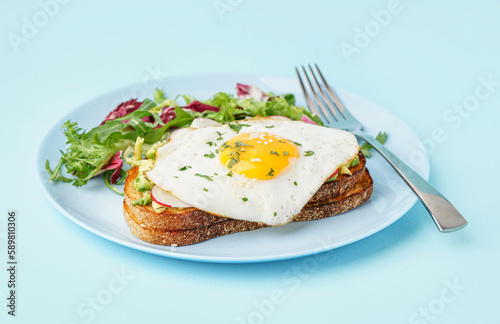 Delicious sandwich with fried egg and salad on blue background