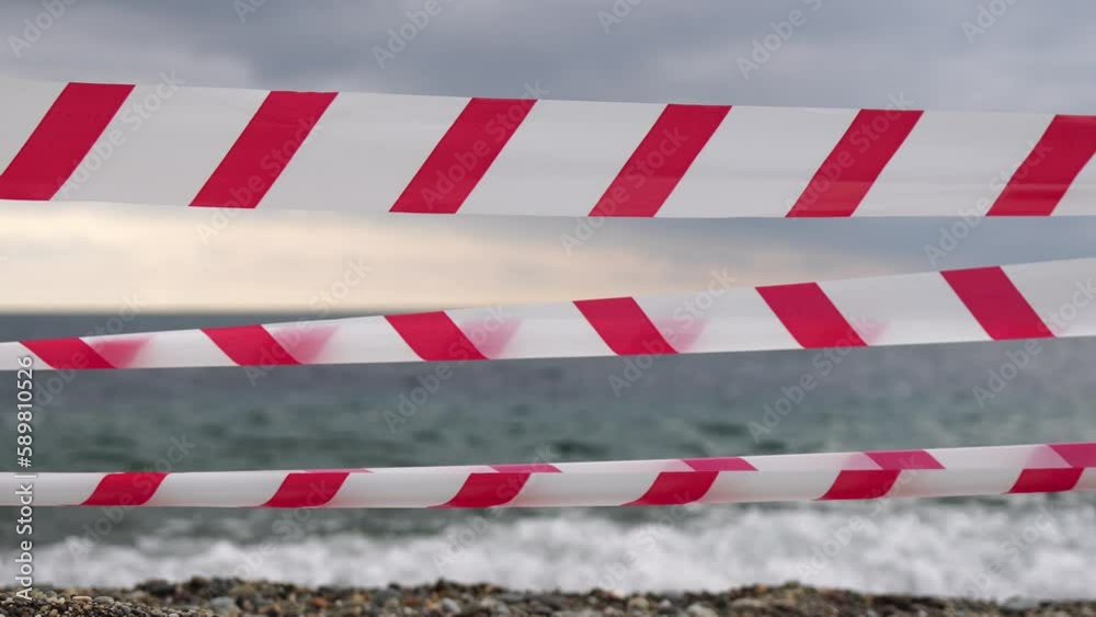 Red white warning tape barrier ribbon swinging in the wind across exotic sea beach background without people. No entry Red White caution tape. No holiday concept, delayed travel, no summer plans Red white warning tape barrier ribbon swinging in the wind across exotic sea beach background without people. No entry Red White caution tape. No holiday concept, delayed travel, no summer plans