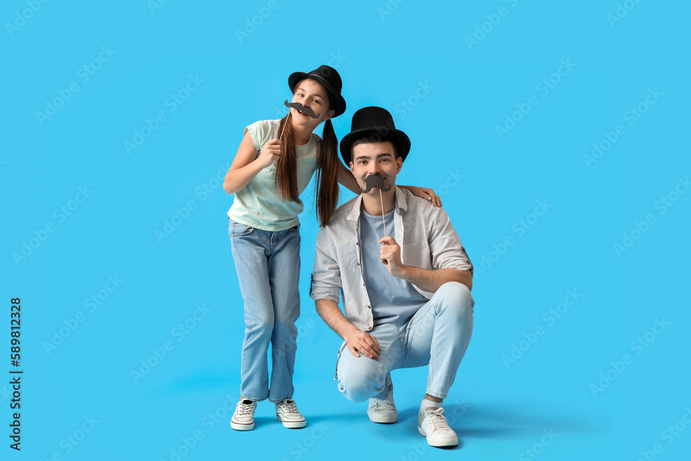 Portrait of father and his little daughter with paper mustache on light blue background Portrait of father and his little daughter with paper mustache on light blue background