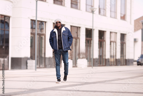 Serious modern fashion man in stylish denim clothes walks in urban street, full length