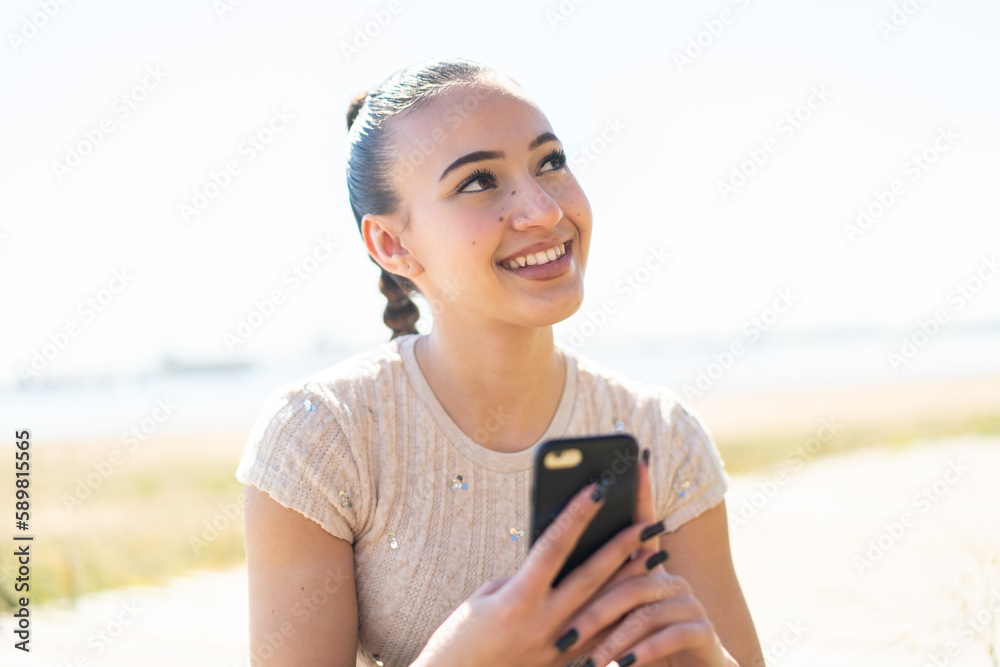 Young moroccan girl  at outdoors using mobile phone and looking up