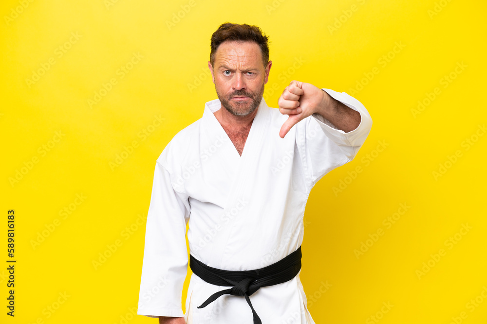 Fototapeta premium Middle age caucasian man doing karate isolated on yellow background showing thumb down with negative expression