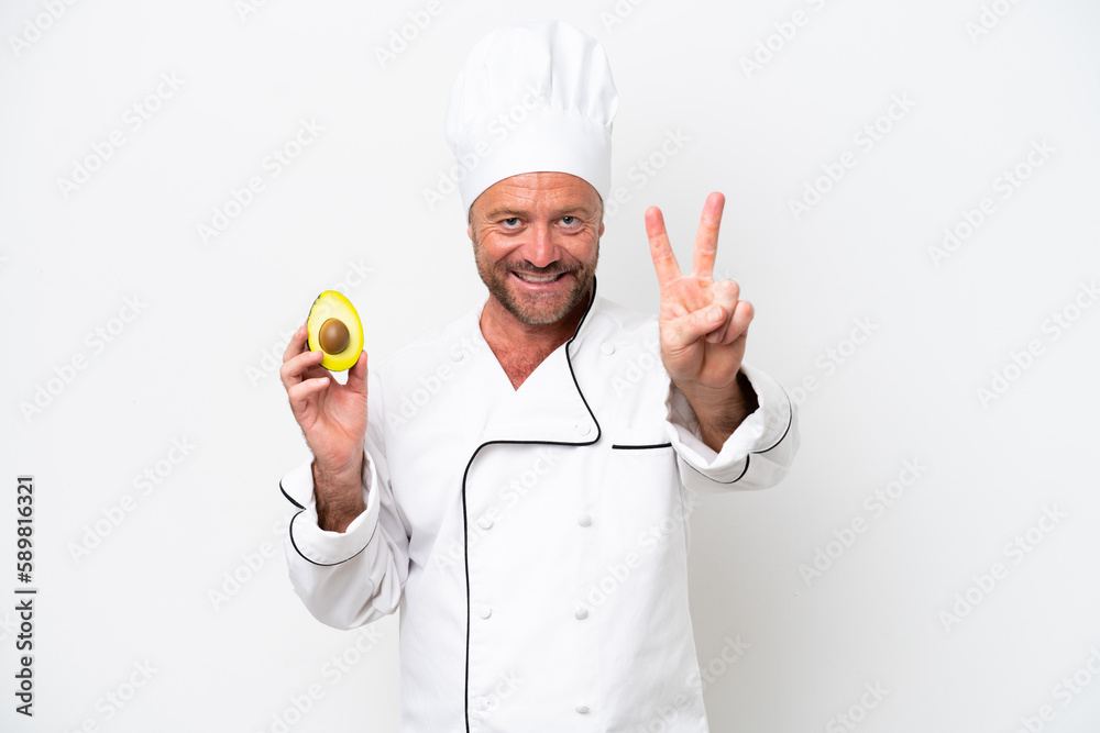 Chef man holding an avocado isolated on white background smiling and showing victory sign