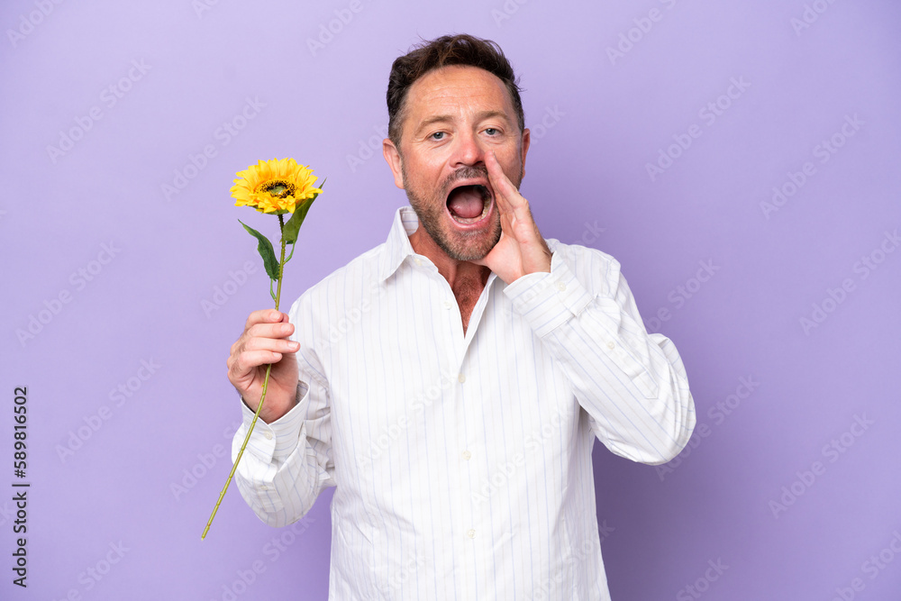 Middle age caucasian man holding sun flower isolated on purple background with surprise and shocked facial expression Middle age caucasian man holding sun flower isolated on purple background with surprise and shocked facial expression