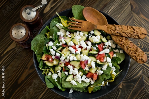 Top view of a colorful and good-looking salad with a wooden spoon and fork near the spice containers