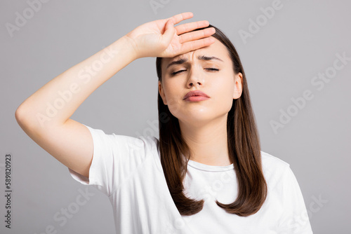 Young beautiful brunette woman wearing white t-shirt over grey isolated background suffering from headache desperate and stressed because pain and migraine. Hands on head.