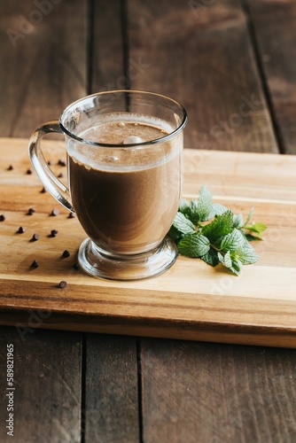 Vertical shot of a glass of hot chocolate on a wooden board with chocolate candies and mint leaves