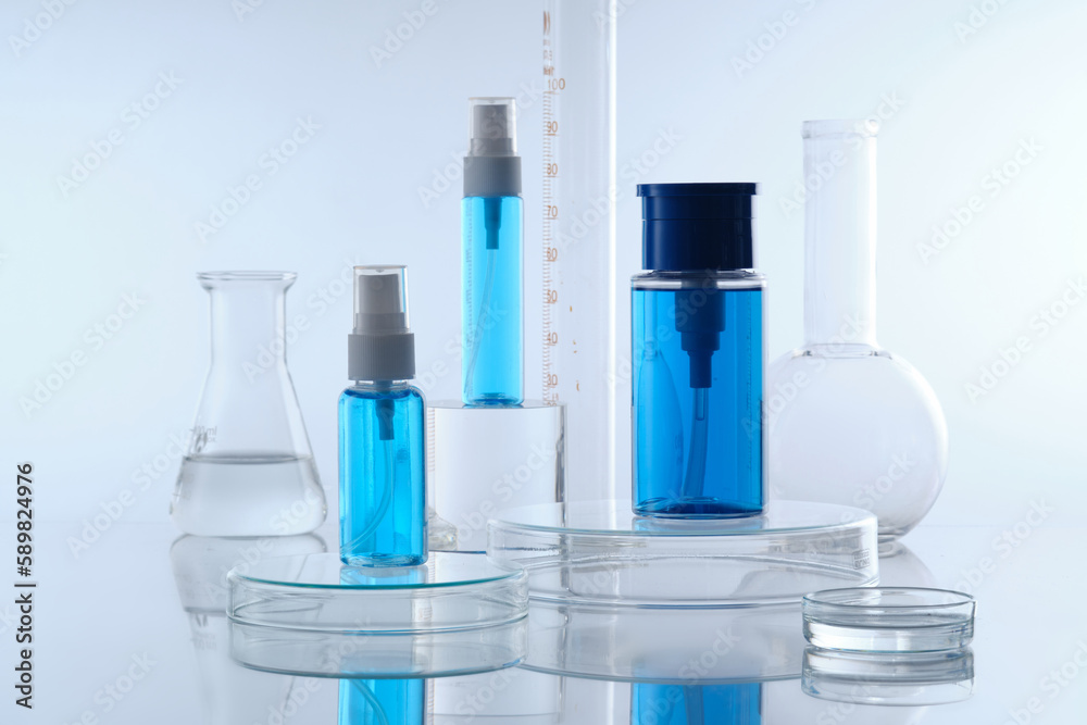 Mockup scene for cosmetic with three blue spray bottle without label placed on transparent podium and laboratory glassware filled colorless liquid decorated on white background. Front view, copy space Mockup scene for cosmetic with three blue spray bottle without label placed on transparent podium and laboratory glassware filled colorless liquid decorated on white background. Front view, copy space