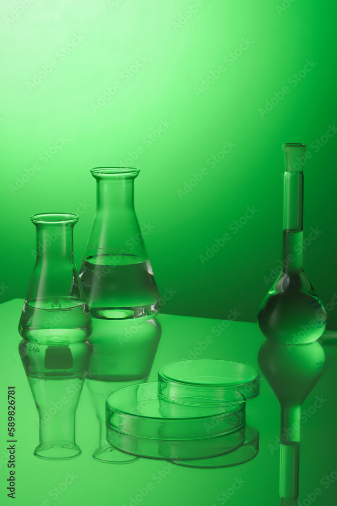 Minimal background with boiling flask and erlenmeyer flask containing transparent liquid inside and petri dishes upside down form an empty platform to display products. Laboratory concept.