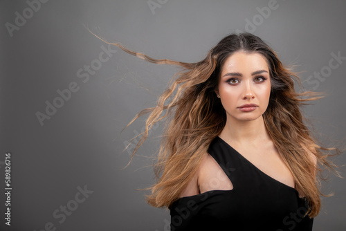 Beauty salon. Beautiful female model with flowing hair, with open shoulders, looks at camera on gray background.