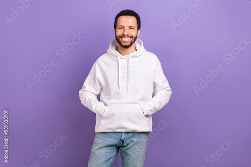 Portrait of pleasant handsome nice guy with brunet beard wear white pullover standing arms in pockets isolated on violet color background © deagreez