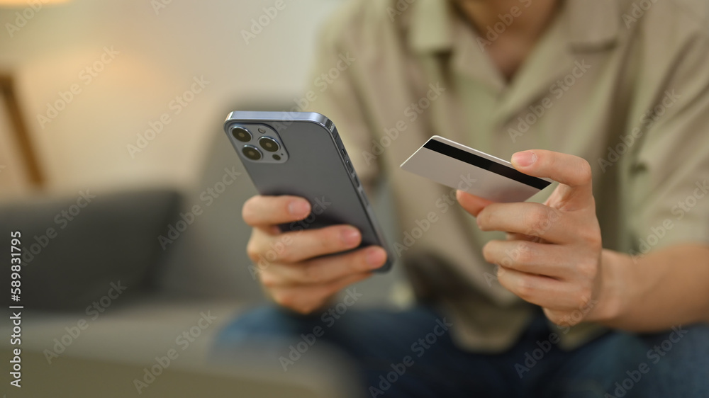Cropped image of man hand holding credit card making transaction or using mobile bank application Cropped image of man hand holding credit card making transaction or using mobile bank application