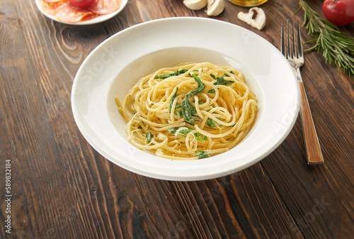 Spaghetti pasta with spinach and parmesan cheese in a white plate on wooden background. Healthy food concept with ingredients