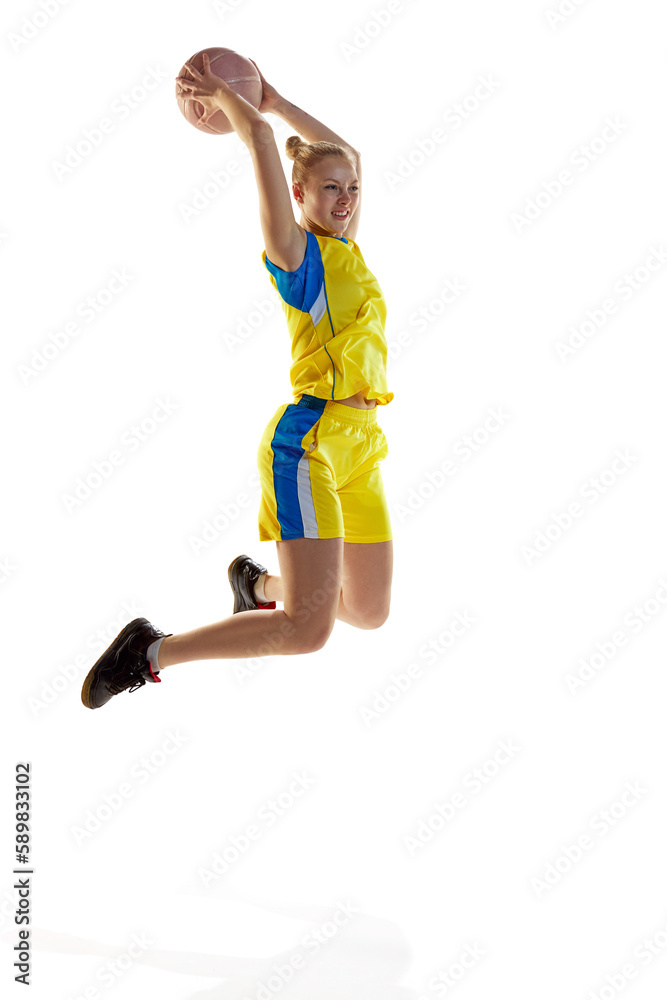 Motivated, concentrated young girl in motion, jumping with ball, playing basketball against white studio background. Concept of professional sport, hobby, healthy lifestyle, action and motion