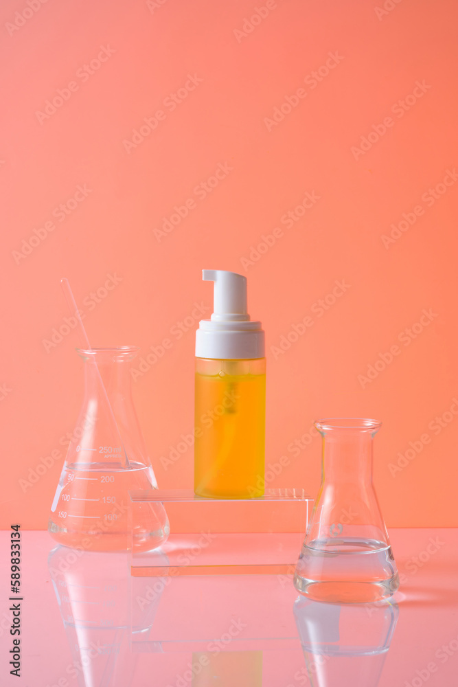 Front view of yellow plastic pump bottle mockup for cosmetic on cylindrical transparent podium and two erlenmeyer flask containing liquid decorated on orange background. Space for design Front view of yellow plastic pump bottle mockup for cosmetic on cylindrical transparent podium and two erlenmeyer flask containing liquid decorated on orange background. Space for design