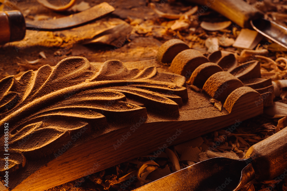 Art wood carving. Carved wooden big leaf on wooden background with shaving. Chisels on background.