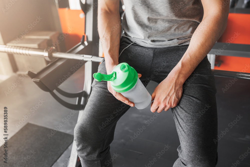 Sports man holding a bottle of water sitting resting after training close-up.