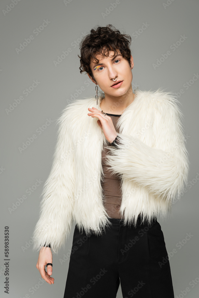 fashionable nonbinary person in white faux fur jacket looking at camera isolated on grey. fashionable nonbinary person in white faux fur jacket looking at camera isolated on grey.