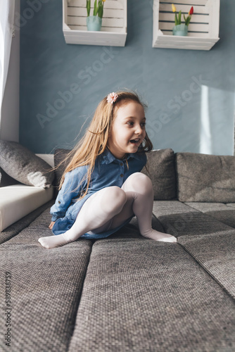 Happy little girl playing on couch at home.