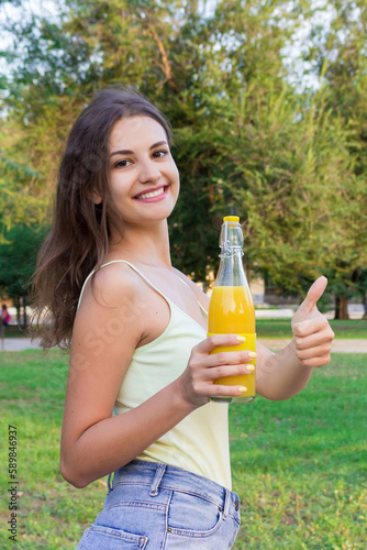Cute girl is having a walk in the park holding a bottle of orange juice in a sunny wam day