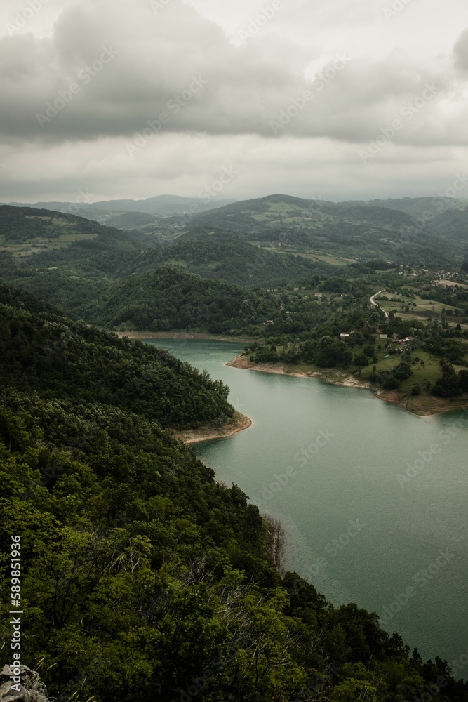Aerial view of Rovni Lake surrounded by green vegetation under gray cloudy sky in western Serbia Aerial view of Rovni Lake surrounded by green vegetation under gray cloudy sky in western Serbia