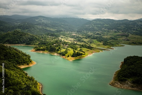 Aerial view of Rovni Lake surrounded by green vegetation under gray cloudy sky in western Serbia