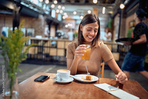Cheerful young woman in coffee shop, enjoying her breakfast and coffee while taking notes.