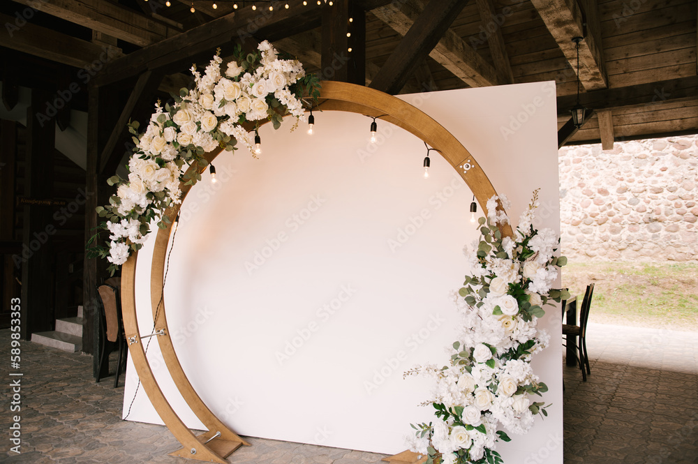 Round wooden arch with white background and decorated with flowers and retro garland