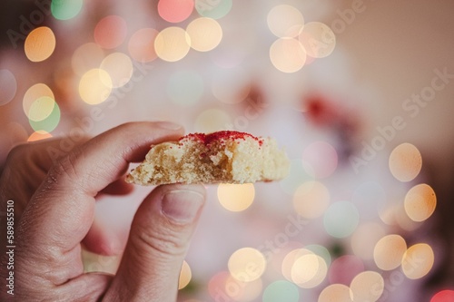 Hand holding a Christmas cookie with sprinkles and bokeh lights in the background