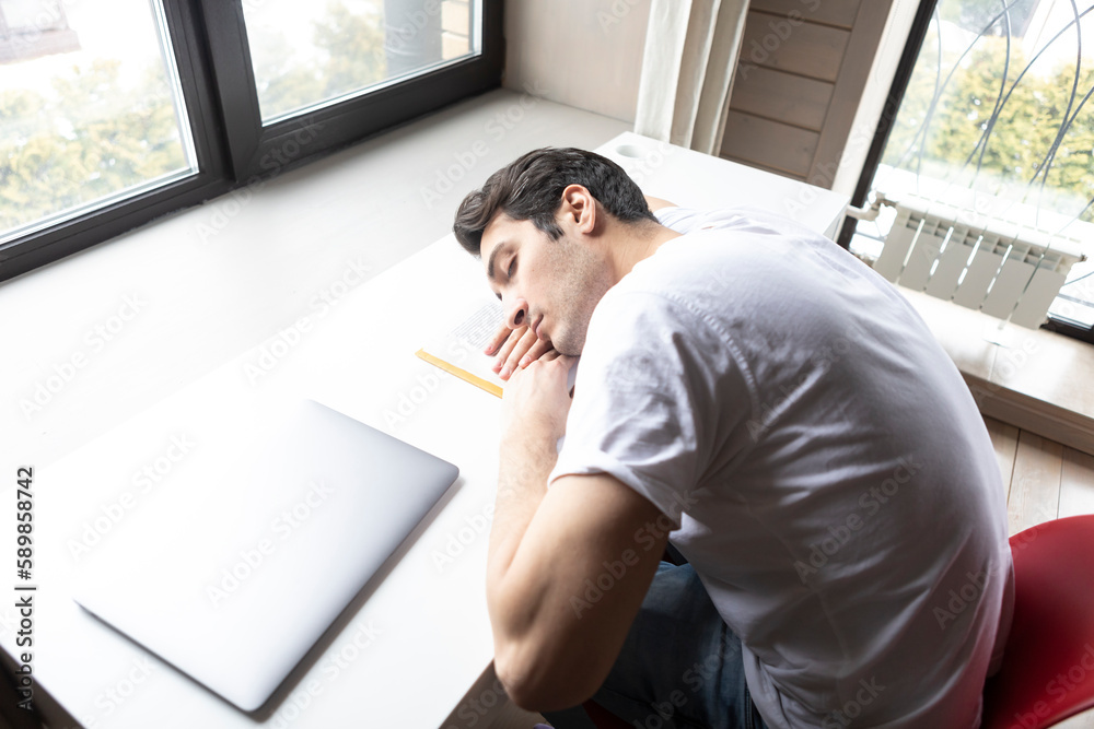Tired and bored student sleeping on the desk while preparing for exams Tired and bored student sleeping on the desk while preparing for exams