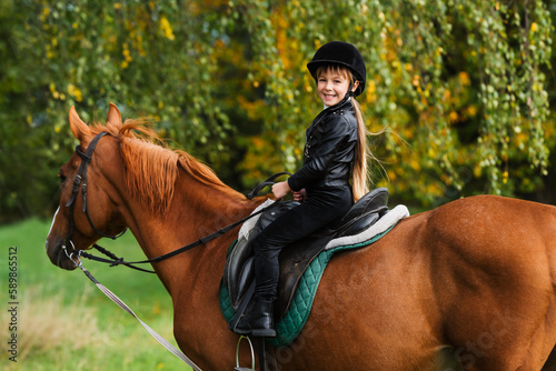 Little girl in jockey outfit rides bay horse. School of riding and equestrian sports.
