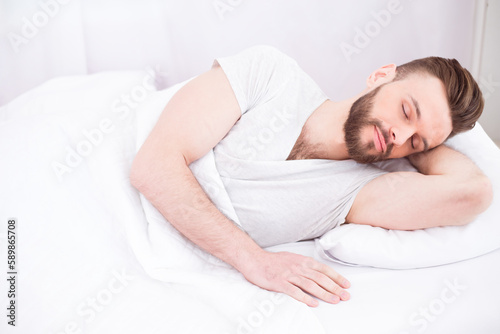 Bed and rest time. Tired millennial handsome bearded man asleep  resting peacefully in white comfortable bed in bedroom  copy space. Relax  sleep  nap at home on weekends.