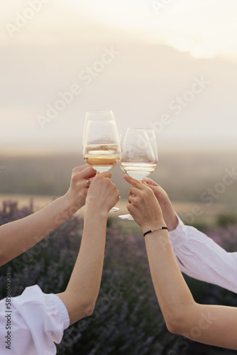 Group of friends with white wine in hands clinking with glasses. Close-up of hands and drinks.