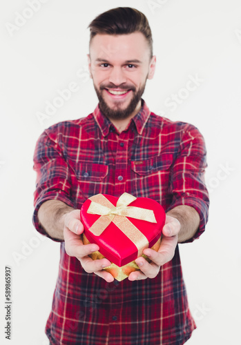 Young handsome man with beard holding present or gift box in hands. Happy birthday, anniversary or Valentine's day