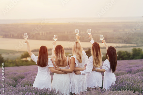 Beautiful girlfriends having picnic in the lavender field in summer sunset. They standing with hands up and enjoying beautiful landscape.