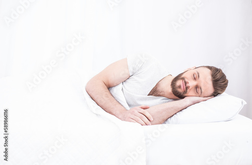 Bed and rest time. Tired millennial handsome bearded man asleep, resting peacefully in white comfortable bed in bedroom, copy space. Relax, sleep, nap at home on weekends.
