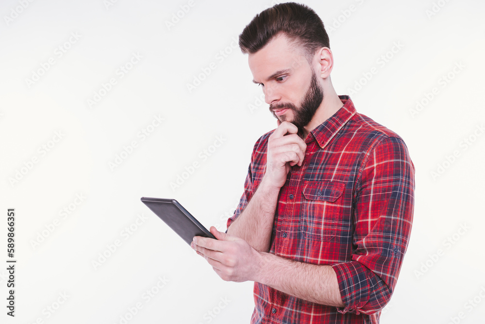 Close up photo of happy young bearded man in plaid shirt standing and using tablet isolated on white background Close up photo of happy young bearded man in plaid shirt standing and using tablet isolated on white background