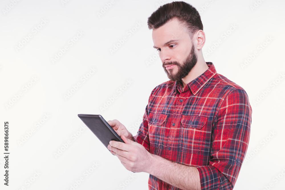 Close up photo of happy young bearded man in plaid shirt standing and using tablet isolated on white background Close up photo of happy young bearded man in plaid shirt standing and using tablet isolated on white background