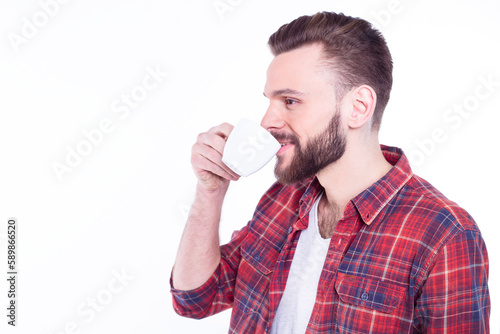 Rest and coffee break. Bearded handsome young man in checkered shirt holding coffee or tea cup and smiling while standing against white background