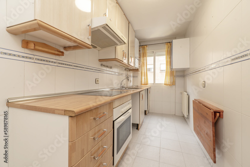 Small kitchen furnished without washing machine or dishwasher with wooden folding table and window with yellow curtains