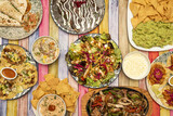 Some typical Mexican dishes with nachos with guacamole and meat, ceviche, chicken salad, wire stew, assorted tacos, burritos and quesadillas on a light wooden table
