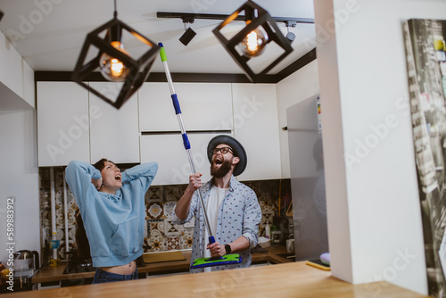 A young couple is looking at the ceiling and screaming while holding a mop because the upstairs neighbor is having a party with loud music or doing repairs in the apartment, workers are drilling with