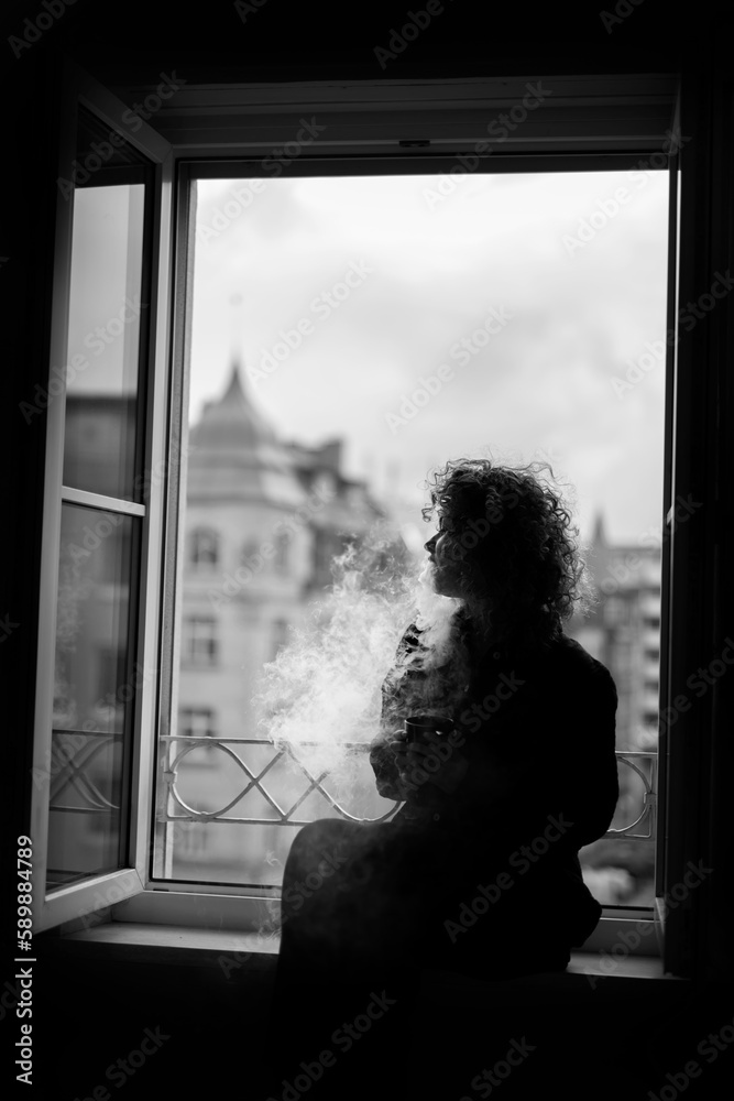Black and white photo of smoking woman near the window
