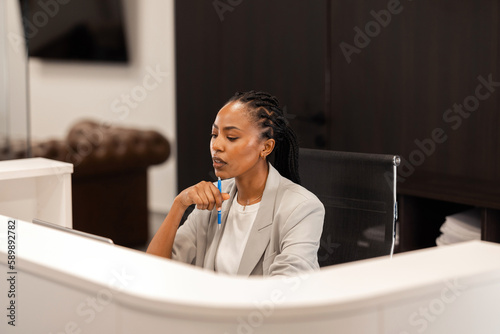 The young African-American female receptionist sits behind the reception desk and waits for the guests.