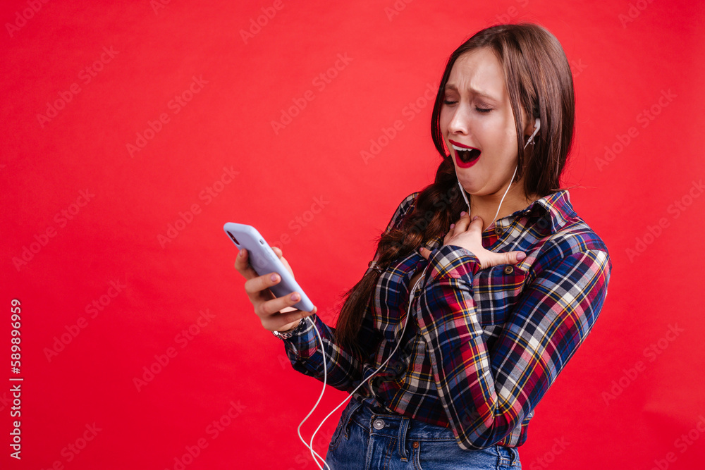 Naklejka premium Laughing girl looking at the screen of the phone while standing on a red background