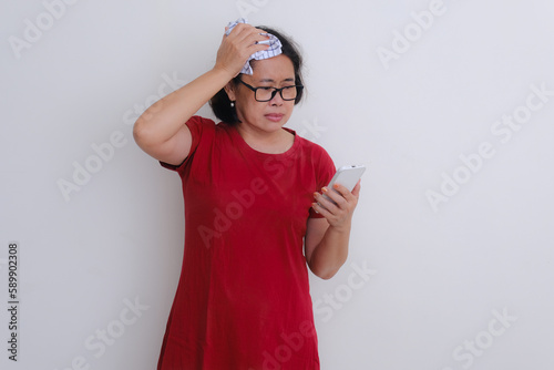 A woman watching something on her smartphone while one hand is on her head; serious expression. photo