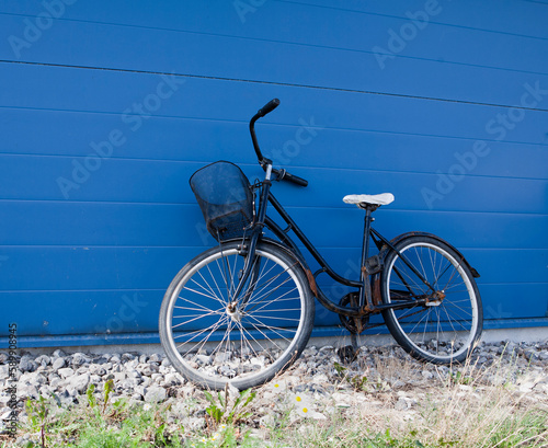 Abandoned old and rusty bicycle parked in front of a blue wall.
