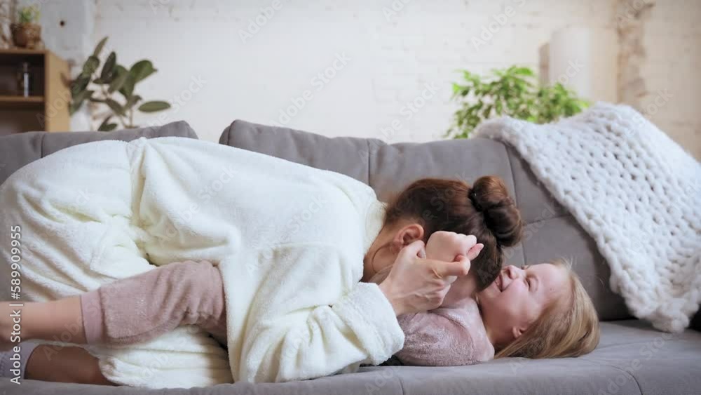Cuddles and kisses. Young woman, happy mother playing with little girl, daughter on sofa at home on daytime. Concept of family relationship, motherhood and childhood, love, caring Cuddles and kisses. Young woman, happy mother playing with little girl, daughter on sofa at home on daytime. Concept of family relationship, motherhood and childhood, love, caring